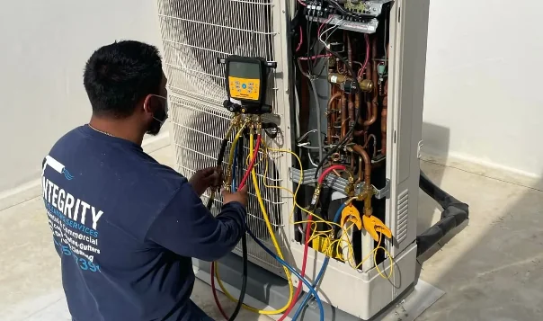 Technician testing refrigerant pressure on outdoor HVAC unit with manifold gauge set