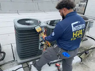 HVAC technician testing outdoor condenser unit with electrical diagnostic equipment